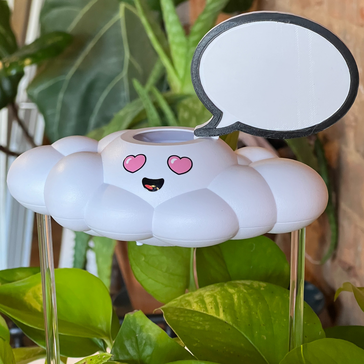 Chloe the cloud with blank word bubble charm, surrounded by green plants.