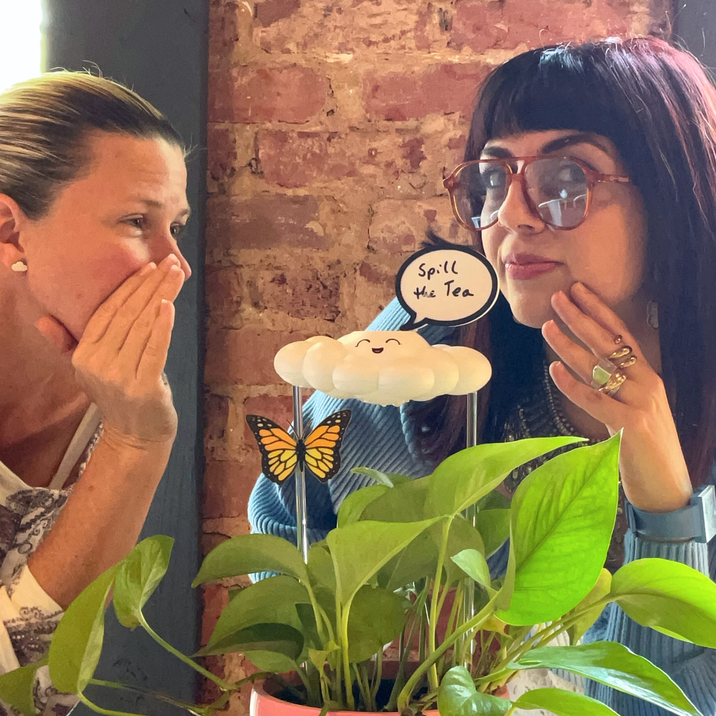 Two women engaged in a conversation with a Chelsea the Cloud and butterfly in the foreground.