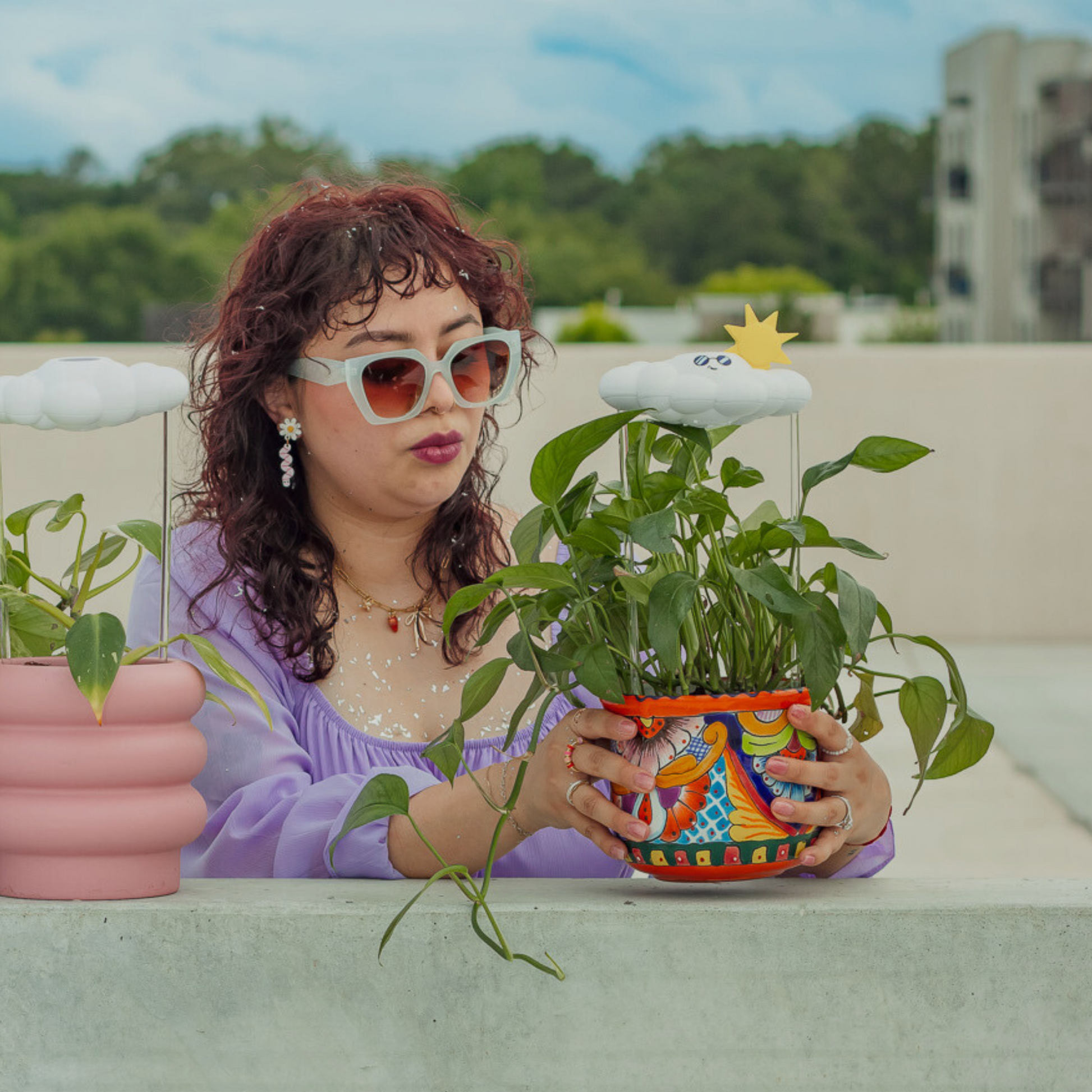 Woman holding a potted plant with Cooper the Cloud on a rooftop with greenery and buildings in the background