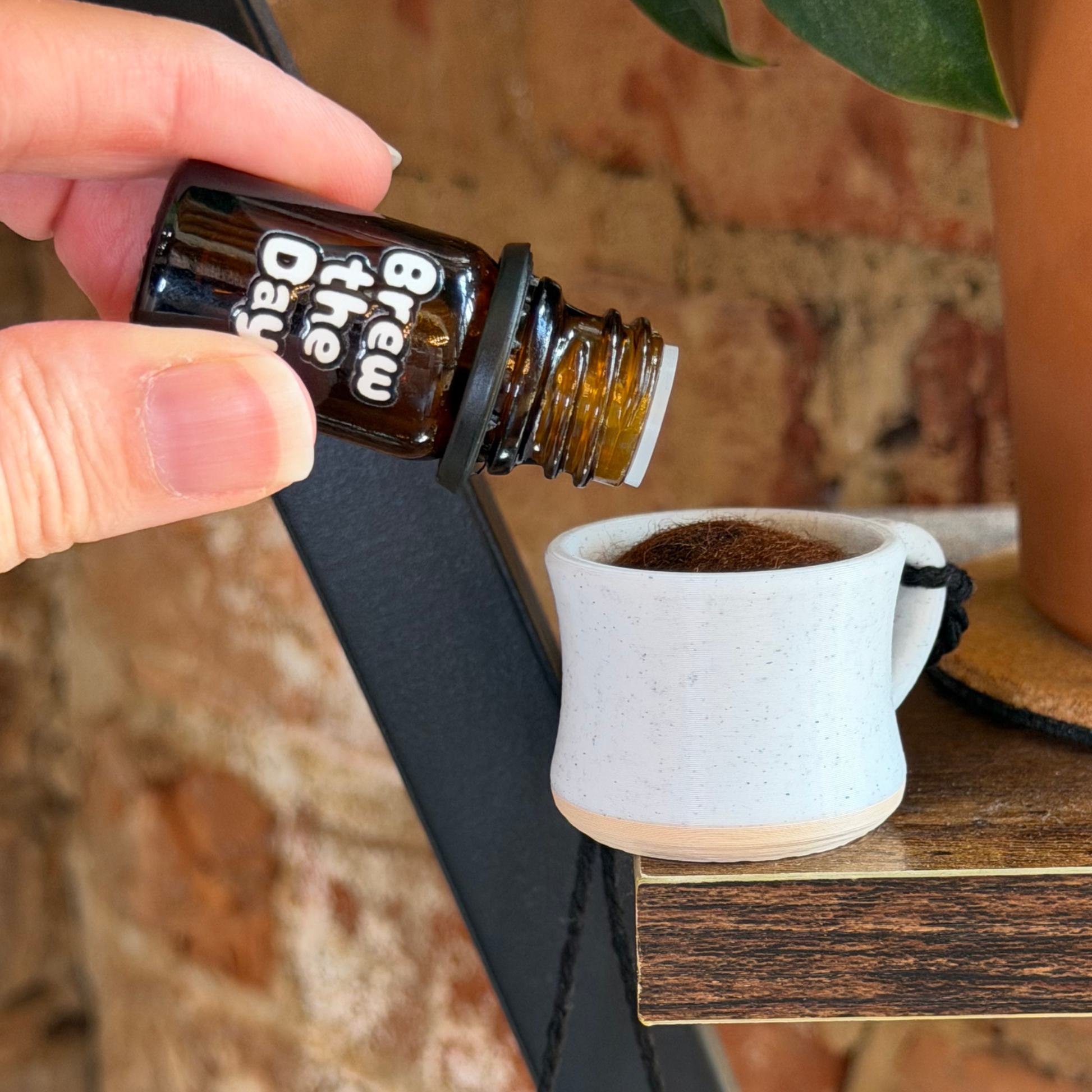 Hand holding a small bottle labeled 'Brew the Day' above a coffee mug diffuser