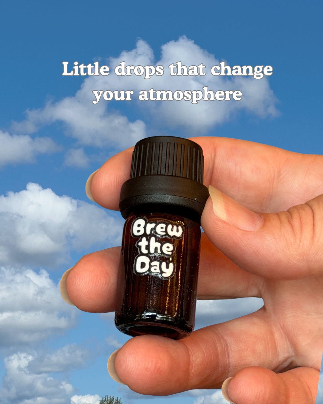Hand holding a small brown bottle labeled 'Brew the Day' against a blue sky with clouds.