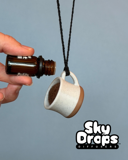 Hand holding a small coffee cup diffuser on a gray background, featuring the brand 'Sky Drops'.